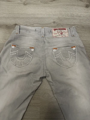 Grå True Religion jeans - Säljer ett par grå jeans från True Religion och jeansen har en rak passform och är tillverkade i mjukt jeanstyg. Storlek 29 men sitter som storlek 26