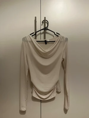 Vit långärmad topp med draperad hals - Stilren vit långärmad topp med snygg draperad halsringning och figurnära passform. Tillverkad i mjukt och stretchigt material som känns bekvämt mot huden. Från HM. Endast testad!