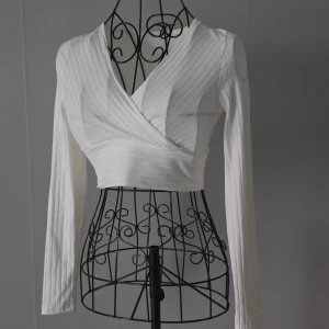 Vit omlott croppad långärmad topp - En trendig topp i croppad modell med omlott-design och v-ringning. Perfekt att styla med höga jeans eller kjol för en modern och trendig look 👌. Använd endast en gång och i mycket fint skick. Säljes då jag rensar i garderoben