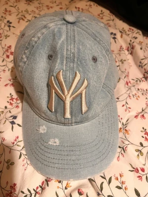 Ljusblå denimkeps med MY-brodyr - Säljer en ljusblå keps i denim-look med stor beige MY-brodyr framtill. Kepsen är i 100% bomull och har klassisk böjd skärm samt ventilationshål. One size fits all. Perfekt för dig som vill ha en streetstyle vibe. Funkar till allt!😊