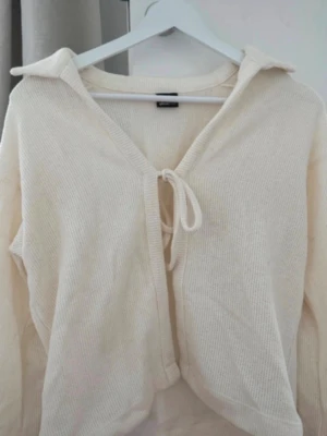 Krämvit ribbad kofta från Gina Tricot - Säljer en krämvit ribbad kofta från Gina Tricot med knytning framtill och bred krage. Koftan har lång ärm och är gjord i mjukt stickat material, perfekt för lager på lager och en chill look🫶🏼