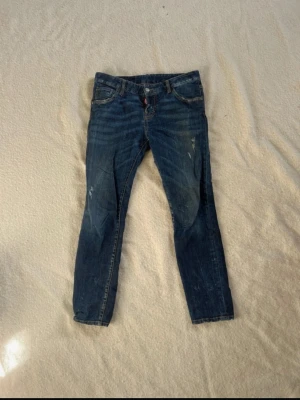 Blå jeans från Dsquared2 - Säljer ett par blå jeans från Dsquared2 med klassisk modell och snygga slitningar. Jeansen har en rak passform och detaljerade sömmar. Perfekta för dig som gillar en avslappnad men trendig stil.