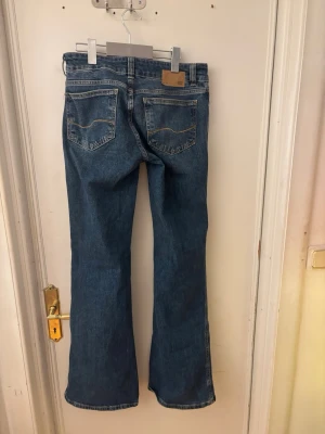 Blå bootcut jeans med hål 157 - Snygga blå bootcut jeans från 157 med slitna hål på båda knäna och klassiska bakfickor. Jeansen har en låg midja och är tillverkade i denim med en cool tvätt. Perfekta för en avslappnad och trendig stil.