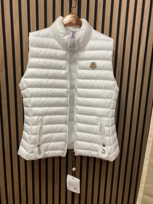 Vit dunväst - Snygg vit dunväst  med quiltad design och hög krage. Västen har dragkedja framtill, två fickor med dragkedja . Perfekt för lager på lager och ger en clean look till din outfit.