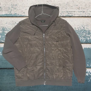 Olivgrön cardigan jacka från Massimodutti  - Snygg olivgrön cardigan jacka från Massimodutti med dragkedja framtill och quiltad front. Tröjan har huva med dragsko, ribbade muddar och mjuka ärmar i sweatshirtmaterial. Perfekt för en avslappnad och trendig look. Modellen är 185 cm och väger 70kg 