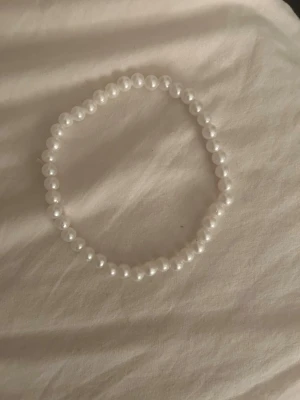 Vitt pärlarmband - Säljer ett stilrent armband med vita pärlor trädda på elastisk tråd. Armbandet har en klassisk rund form och passar perfekt för dig som gillar enkel men snygg design. Inget synligt märke på armbandet.