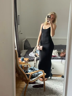 Svart långklänning med smala axelband - Säljer en stilren svart långklänning med smala axelband och figurnära passform. Klänningen är ärmlös och har en enkel, klassisk design som passar perfekt till många tillfällen. Materialet känns mjukt och stretchigt.