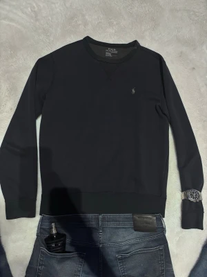 Mörkblå sweatshirt från Polo Ralph Lauren - Klassisk mörkblå sweatshirt från Polo Ralph Lauren med rund halsringning och diskret broderad logga på bröstet. Tröjan har långa ärmar och ribbade muddar vid ärmslut och nederkant. Perfekt för en avslappnad och stilren look.