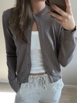 Brun kofta från H&M - Säljer en tunn, brun kofta från H&M med rund halsringning och knäppning framtill. Koftan har långa ärmar och en enkel, stilren design som passar perfekt till lager-på-lager-look. Materialet är mjukt och lätt, vilket gör den skön att bära.