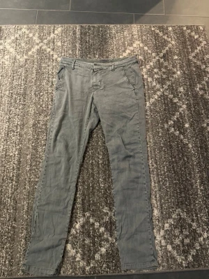 Gråa chinos från Dondup - Snygga grå chinos från Dondup, tillverkade i Italien. Byxorna har en smal passform, klassiska sidfickor och bälteshällor. Perfekta för en avslappnad men stilren look. Helt nya och orörda. Skicket är 5/5 men finns inte prislapp kvar. Ny pris 5000 kr 