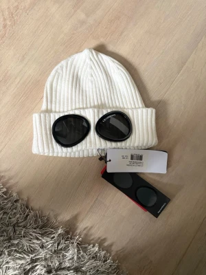 Vit ribbstickad mössa cp company - Snygg vit ribbstickad mössa med uppvikt kant. Klassisk och stilren design som passar perfekt till kalla vinterdagar. Mössan är tillverkad i ett mjukt och värmande material som håller dig varm och bekväm. 