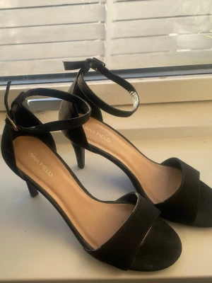 Svarta klackskor från Anna Field - Stilrena svarta pumps från Anna Field med öppen tå och smal ankelrem med spänne. Skorna har en klassisk klack och är tillverkade i mockaimitation. Perfekta för dig som vill ha en elegant och enkel look. Andvända 1 gång, perfekta till bal eller sommarskor 💗💗