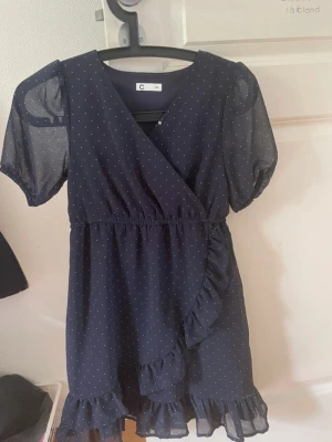 Mörkblå prickig omlottklänning - Söt mörkblå kortklänning med vita prickar och volangdetaljer. Klänningen har omlottmodell, korta puffärmar i transparent material och resår i midjan. Perfekt för dig som gillar en feminin och lekfull stil. Aldrig använts , köpte för 349 kr! 💞