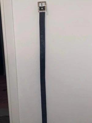 Svart D&G läder skärp med strass - Snyggt svart skärp från D&G i äkta skinn med ett stort fyrkantigt spänne dekorerat med strass. Skärpet har präglad logga längs remmen. Lite tecken på slit då texten på baksidan (som ej syns när du har på dig bältet) är lite utsuddad, och en diamant saknas på spännet.