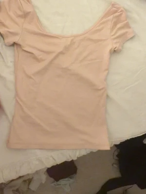Ljusrosa topp från H&M - Säljer en ljusrosa topp från H&M med korta ärmar och bred, djup urringning. Toppen är figurnära och gjord i ett mjukt, stretchigt material som passar perfekt till jeans eller kjol.