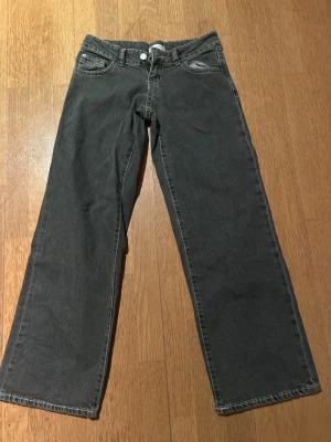Grå raka jeans med låg midja - Snygga grå jeans med rak passform och låg midja. Klassisk femficksmodell med knapp- och dragkedjegylf. Jeansen har en enkel design utan slitningar eller dekorationer, perfekta för en clean och avslappnad stil. Tillverkade i mjukt denimtyg.