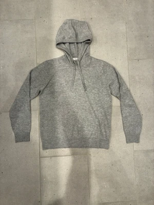 Grå hoodie från RYVLS - Mysig grå hoodie från RYVLS med klassisk huva och dragsnören. Tillverkad i mjukt stickat material som känns skönt mot huden. Perfekt för en avslappnad och stilren look. Långa ärmar och ribbade muddar för extra komfort.