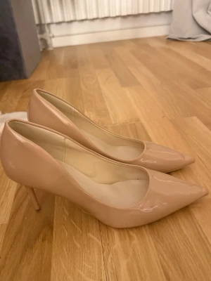 Beige lackpumps  - Säljer dessa snygga pumps i beige lack med spetsig tå och smal klack. Skorna har använts varsamt och är endast synligt använda på sulan, övre delen av skorna har inget tecken på användning. De har en klassisk och elegant design med glansig finish och neutrala toner som passar till många outfits.