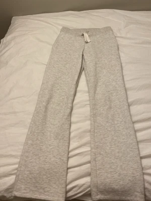 Ljusgråa utsvängda mjukisbyxor - Säljer ett par ljusgrå mjukisbyxor med utsvängda ben och dragsko i midjan. Byxorna är gjorda i mjukt sweatshirtmaterial och har en enkel, clean look utan synliga loggor eller fickor. Perfekta för chill dagar hemma eller när du vill vara extra bekväm.