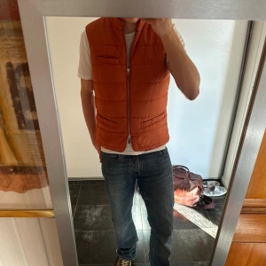 Orange quiltad dunväst med dragkedja - John Henric. Storlek L.Snygg orange quiltad dunväst med dragkedja framtill och flera fickor. 