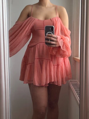 Korall volangklänning med ballongärmar - Säljer en superfin korallfärgad klänning med tunna axelband och stora ballongärmar. Klänningen har flera volanger och en luftig, flowy passform och är i sommarens trendigaste färg. Perfekt för sommarens alla tillfällen, midsommar, födelsedagar och fest!