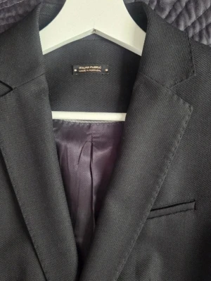 Massimo Dutti  - Stilren svart kavaj från Massimo Dutti italienskt tyg, tillverkad i Portugal. Klassisk passform med spetsiga slag och lila innerfoder. Etiketten med materialinformation är avklippt 