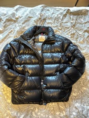 Svart dunjacka från Moncler - Säljer denna moncler jackan för den inte kommer till användning. Har tagit av luvan för det finns ett litet hål i deb på insidan. Det finns även ett ihop limmat hål (litet) som man ser på bild 5. Annars är jacken i väldigt bra skick