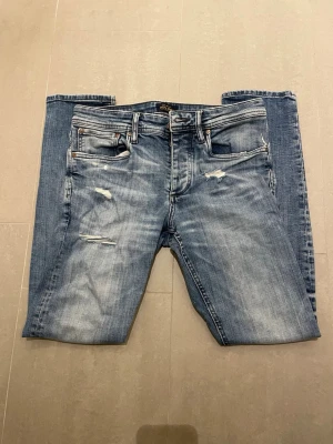 Blå slitna jeans från Jack & Jones - Säljer ett par blå jeans från Jack & Jones med slitningar och distressed detaljer på framsidan. Klassisk femficksmodell med ljus tvätt och raka ben. Säljs för ett mycket bra pris men kan diskuteras. Skriv vid minsta fundering!!🤩🤩🤩
