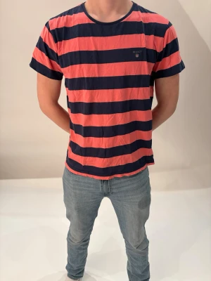 Gant T-shirt  - Snygg t-shirt från GANT med breda marinblå och röda ränder. I storlek M.