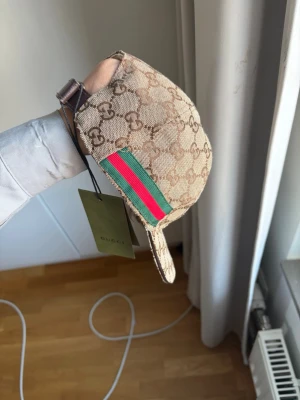 Beige keps med GG-mönster  - Säljer en beige keps från Gucci med det klassiska GG-monogrammet i brunt över hela kepsen. Justerbar rem i brunt läder baktill och detaljer i canvas. Perfekt för dig som vill ha en lyxig och tidlös accessoar till din outfit.