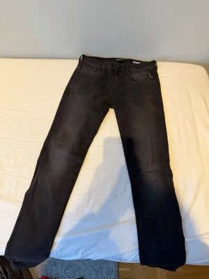 Svarta Replay Anbass Jeans - Säljer ett par svarta jeans från Replay med klassisk femficksdesign och raka ben. Jeansen har en lätt tvättad look och är tillverkade i bomull med lite stretch för extra komfort. Perfekta till en avslappnad stil. Har endast använts 1 gång så inga tecken på användning. W29 L34. Pris kan diskuteras. Modellen är Anbass. 