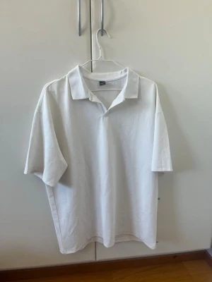 Vit piké med krage - Vit pikétröja med klassisk krage och korta ärmar. Enkel och stilren design, perfekt för en avslappnad look. Tillverkad i ett mjukt material som känns bekvämt mot huden.