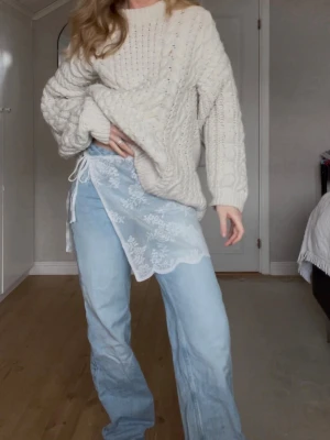 Vit spetskjol med knytband - Säljer en handsydd kort, vit kjol i spets med blommigt mönster och knytband i midjan. Kjolen har en transparent look och vågig kant nertill, perfekt för att styla över byxor eller tights för en trendig lager-på-lager-look. Passar S/M