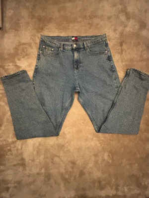 Blå raka jeans från Tommy Hilfiger - Klassiska blå jeans från Tommy Hilfiger med rak passform och fem fickor. Jeansen har en normal hög midja och subtilt stentvättad finish. Tillverkade i 100% bomull för en autentisk denimkänsla. Perfekta för en avslappnad och tidlös look. Byxorna Köptes i butik för nypris (1200kr) och jag säljer byxorna för 350kr, byxorna är i 10/10 skick och har använts ett fåtal gånger. Hör av dig vid minsta fundering