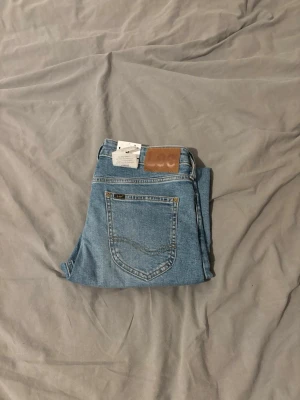 Ljusblå raka jeans från Lee - Säljer ett par ljusblå jeans från Lee med klassisk femficksdesign och raka ben. Jeansen har en snygg läderpatch med Lee-loggan bak i midjan och är gjorda i slitstark denim. Perfekta för dig som gillar en tidlös och clean look. Storlek w30 l30