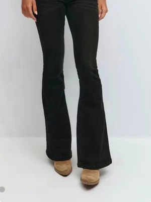 Svarta bootcut jeans med detaljer - Snygga svarta bootcut jeans med utsvängda ben och coola sömdetaljer på bakfickorna. Jeansen har klassisk femficksdesign och är perfekta för dig som gillar en retroinspirerad look. Materialet är stretchigt för extra komfort.