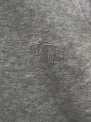 Grå hoodie från Burberry med dragkedja - Snygg gråmelerad hoodie från Burberry med dragkedja framtill och klassisk huva med snörning. Ikoniska Burberry-rutiga detaljer syns i huvan och loggan är diskret broderad på bröstet. Tillverkad i mjuk bomullsblandning för maximal komfort.