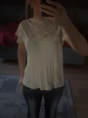 Vit blus med spetsdetaljer - Säljer en söt vit blus med korta ärmar och vacker spets upptill. Blusen har rund halsringning och ett lätt, luftigt tyg som ger en fin look. Säljer nu då den inte används mycket längre, fråga bara om ni vill ha bättre bilder då jag vet att det är dålig kvalité.