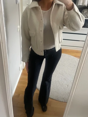 Vår jacka beige - Snygg ljus vår jacka med krage och två stora bröstfickor. Jackan har en rak, något boxig passform och stängs med knappar framtill. Perfekt att slänga över en topp för en clean och trendig look.