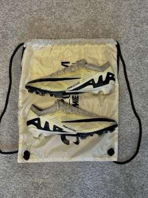 Nike Air Zoom Mercurial fotbollsskor - Säljer ett par Nike Air Zoom Mercurial fotbollsskor i vitt och svart med gula detaljer. Dessa skor ligger nu pris på 2 800 kr då det är modellen elit där du även får med dig påsen på köpet. Skorna har en låg profil, snörning och en lätt ovandel i syntetmaterial. Sulan har fasta dobbar för spel på gräs och AIR- och ZOOM-loggor på sidorna och undersidan. Skorna är st 44 och säljer för de är för små. Priset kan diskuteras så skriv vid minsta lilla fundering 👍