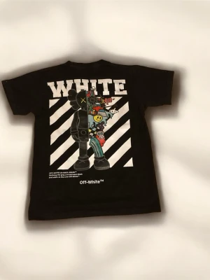 Svart Off-White t-shirt med tryck - Säljer en svart t-shirt från Off-White med stort grafiskt tryck på ryggen och mindre tryck fram. T-shirten har bra passform och korta ärmar. Materialet är mjuk bomull och designen har coola detaljer med figurer och logga.