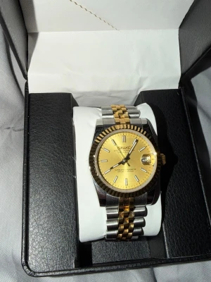 Seikomod’Datejust’ klocka  - Säljer en riktigt snygg Seiko mod med guldfärgad tavla och tvåtonslänk (guld/silver). Klockan är helt ny / i princip oanvänd och i toppskick.  Jag har tagit bort några länkar för att passa min handled, men självklart följer alla originaldelar/länkar med så den går att justera till önskad storlek.  🔹 Automatisk 🔹 Datum med cyclops 🔹 Tvåtonslänk (jubilee-stil) 🔹 Guld tavla med fluted bezel-look 🔹 Nypris: 2800 kr  Perfekt om du vill ha en stilren klocka med lyxig känsla till bra pris.