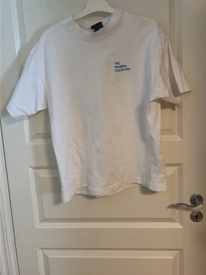 Vit t-shirt med Tryck  - Vit t-shirt från H&M med tryck fram och stort grafiskt tryck på ryggen med palmer och hus. Klassisk passform och rund hals. Perfekt för dig som gillar stilrena plagg med en twist. Materialet känns mjukt och skönt mot huden.