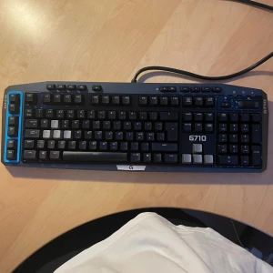 Logitech G710 mekaniskt tangentbord - Säljer ett svart och blått Logitech G710 mekaniskt tangentbord med vita och gråa tangenter. Tangentbordet har full storlek, numerisk del och dedikerade makroknappar. Perfekt för gaming och produktivitet, ansluts via USB-kabel.