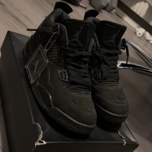 Svarta Air Jordan 4 Retro sneakers - Säljer ett par svarta Air Jordan 4 Retro sneakers med ikoniska Jumpman-loggor på plös och häl. Skorna har meshpaneler, mockaliknande material och plastdetaljer vid snörningen. Klassisk siluett med högt skaft och robust yttersula. Perfekta för dig som gillar streetwear.
