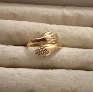 Guldfärgad ring med handmotiv - Unik guldfärgad ring i metall med två händer som möts framtill. Ringen har en modern och konstnärlig design som sticker ut och passar perfekt för dig som gillar personliga accessoarer. Justerbar storlek för bästa passform.