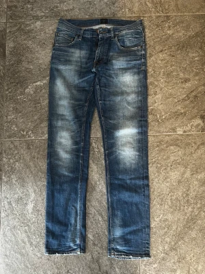 Blå slitna jeans med raka ben - Säljer ett par blå jeans med snyggt slitna detaljer och raka ben. Jeansen har klassisk femficksdesign, normal midja och ljusare partier på lår och knän för en cool, använd look. Perfekta för dig som gillar en avslappnad stil.