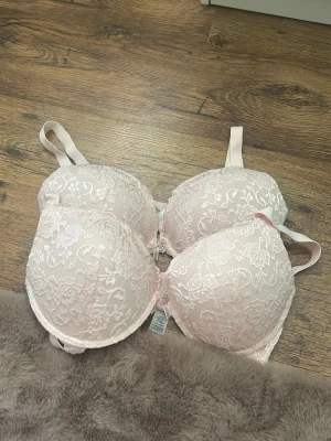 Ljusrosa spets-bh med rosett - Söt ljusrosa bh med vadderade kupor och vacker spets över hela ytan. Mellan kuporna sitter en liten rosett med ett silverfärgat hänge. Justerbara axelband och mjukt material för extra komfort. Från cubus (bella push up) F75. Använd max 2 gånger.       Nypris:249 styck!