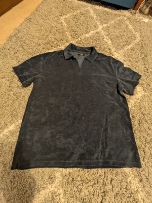 Blå frottéskjorta från Jack & Jones - Säljer en blå skjorta från Jack & Jones Premium i frottématerial. Skjortan har korta ärmar, klassisk krage och v-ringad öppning framtill. Perfekt för dig som gillar en avslappnad och cool stil.