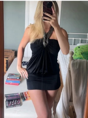 Svart kort klänning med pärldetaljer - Svart kort klänning med halterneck och snygga pärldetaljer framtill. Klänningen har en öppen rygg med knytband i nacken och en draperad front. Otroligt stretchig, står ingen storlek men skulle gissa på small eller medium🌻